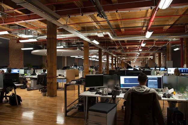 rows of desks and computers with people working in the open concept converted factory office of Ubisoft Toronto
