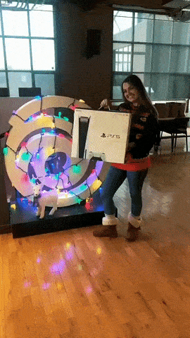 GIF of Breanna Harvey holding PlayStation 5 in front of Ubisoft Logo decorated with holiday lights